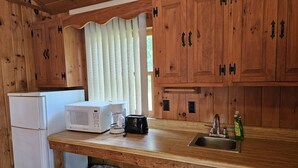 A compact kitchen with wooden cabinets, a white refrigerator, a microwave, a coffee maker, and a sink. - The Gold Eagle Cottage 16 (Lake George)