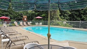 Un área de piscina con sillones de descanso, sombrillas y una mesa.