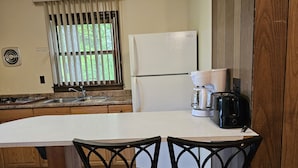 Una cocina con un refrigerador blanco, una cafetera y un tostador sobre la encimera. Hay dos sillas con un diseño singular.