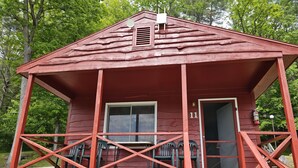 A red wooden cabin with a porch, a window, and a door.