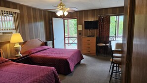 A room with two beds, a desk with a TV, a chair, and a window with a view of greenery.