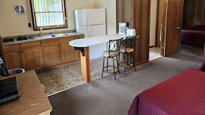 A compact kitchen with wooden cabinets, a white refrigerator, a coffee maker, and a sink. There is a small dining area with two chairs and a table.