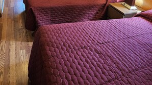 Une chambre avec deux lits, un bureau avec une chaise, une télévision et une fenêtre avec des rideaux.