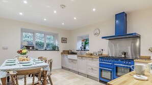 Een moderne keuken met een blauwe kookplaat, witte kasten, en een eetgedeelte met houten stoelen en een tafel voor vier personen.