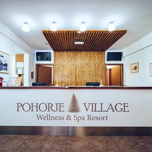 A reception desk at Pohorje Village Wellness & Spa Resort with a wooden panel wall, two TVs, and a logo. - Apartments Bolfenk (Maribor)