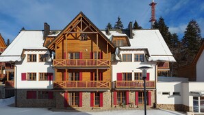 Un immeuble en bois à plusieurs étages, doté de balcons, de murs en pierre et de volets rouges.