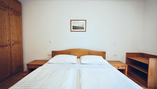 Une chambre avec deux lits, une tête de lit en bois, une table de chevet, une armoire en bois et un tableau encadré au mur.