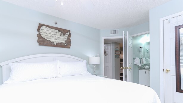A bedroom with a bed, a wall map, a door to a bathroom, and a closet. - Royal Palms 502 by Liquid Life (Gulf Shores)