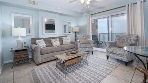 A living room with a sofa, armchair, coffee table, and a glass door leading to a balcony. - Royal Palms 502 by Liquid Life (Gulf Shores)