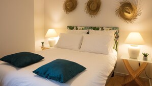 A neatly made bed with white linens and two teal pillows, flanked by two wall-mounted lamps and a small potted plant on a wooden nightstand. - Superb apartment in the city center (Tournus)
