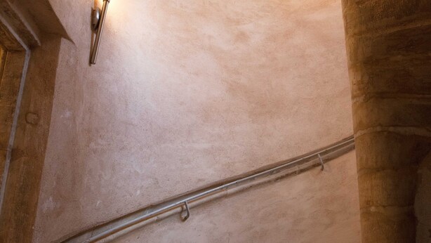 A spiral staircase with a handrail, a wall-mounted light, and a stone wall. - Superb apartment in the city center (Tournus)