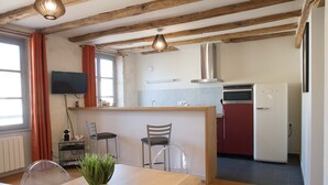 A modern kitchen with wooden beams, a dining area with a table and chairs, and a TV mounted on the wall. - Superb apartment in the city center (Tournus)