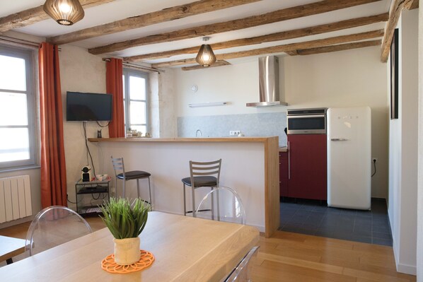 A modern kitchen with wooden beams, a dining area with a table and chairs, and a TV mounted on the wall. - Superb apartment in the city center (Tournus)