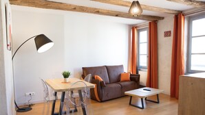 A modern living room with a wooden floor, a brown sofa with orange cushions, a clear dining table with chairs, and a floor lamp. - Superb apartment in the city center (Tournus)