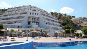 A multi-story hotel with a pool area, including sun loungers and umbrellas.