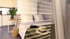 A bedroom with a bed, a bedside table, a suitcase, a hat, and a plant.