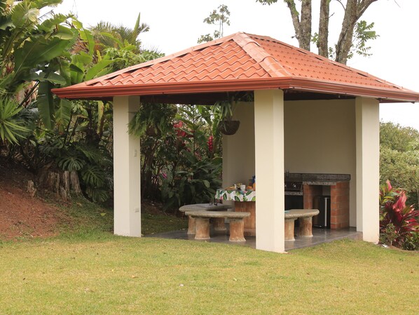 A covered outdoor area with a tiled roof, a barbecue grill, and a table with chairs.