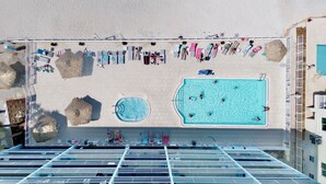 A rooftop pool area with multiple swimming pools, lounge chairs, and umbrellas.