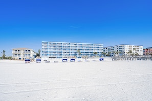 A beachfront hotel with multiple floors, a sandy beach in front, and a clear blue sky.