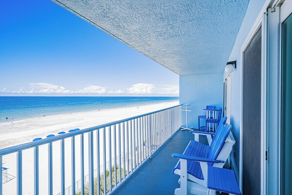A balcony with blue chairs overlooking a beach.