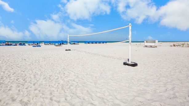 Una cancha de voleibol de playa con una red, sillas azules y una estructura blanca al fondo.