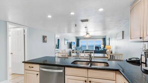 Una cocina con una isla central, lavavajillas y pileta. Se observa un comedor con sillas y una mesa al fondo.