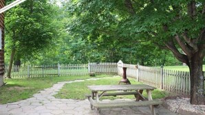 A picnic area with a wooden table and benches, surrounded by a white picket fence and lush greenery. - Gettysburg Getaway! Battlefields/Wineries/Ski! (Orrtanna)