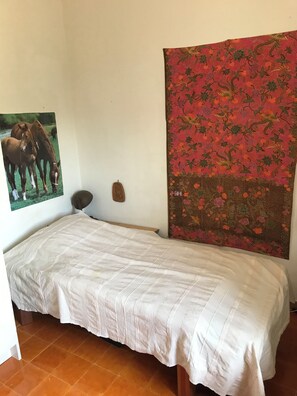 A small, neatly made bed with a white bedspread in a room with a tiled floor.