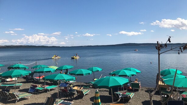 A beach with rows of green umbrellas and lounge chairs, a clear sky, and a calm sea with boats. - 2-storey vacation home with 2 large terraces and sensational views (Mazzano Romano)