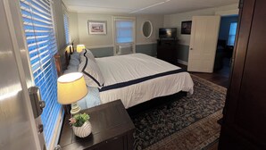 Un dormitorio con cama, lámparas de noche, cómoda, televisor y puerta que da a otra habitación.
