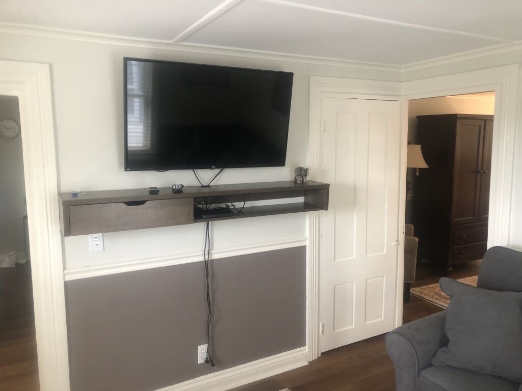 Un soggiorno con TV a parete, un divano grigio e una porta che dà su un'altra stanza.