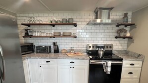 Una cocina moderna con armarios blancos, electrodomésticos de acero inoxidable y estantes de madera.