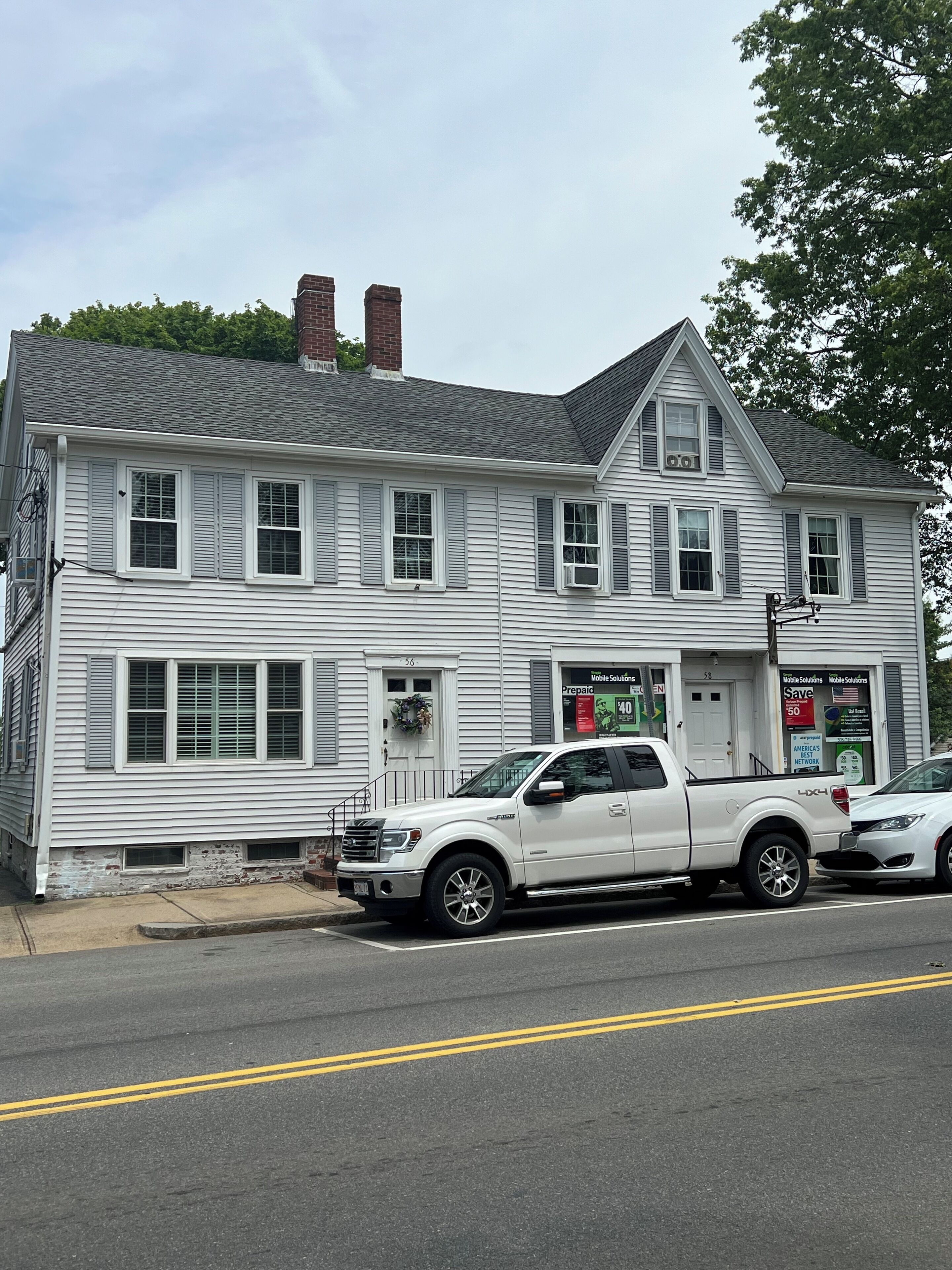 A two-story white building with a garage, a driveway, and a street.