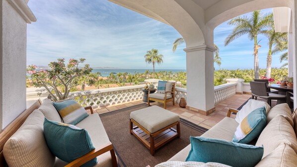 A balcony with a view of the ocean, furnished with a sofa, chairs, and a table.