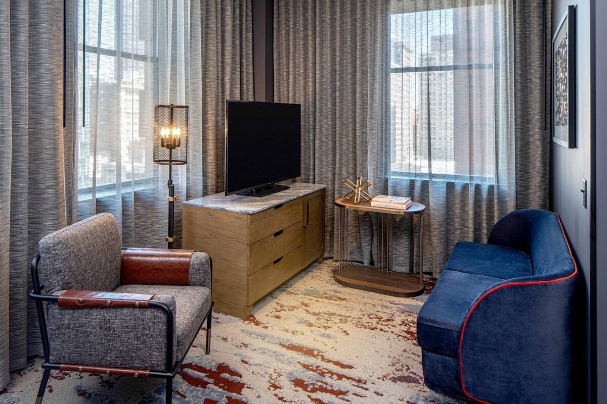 A modern hotel room with a flat-screen TV, a wooden cabinet, a small round table, and two chairs.