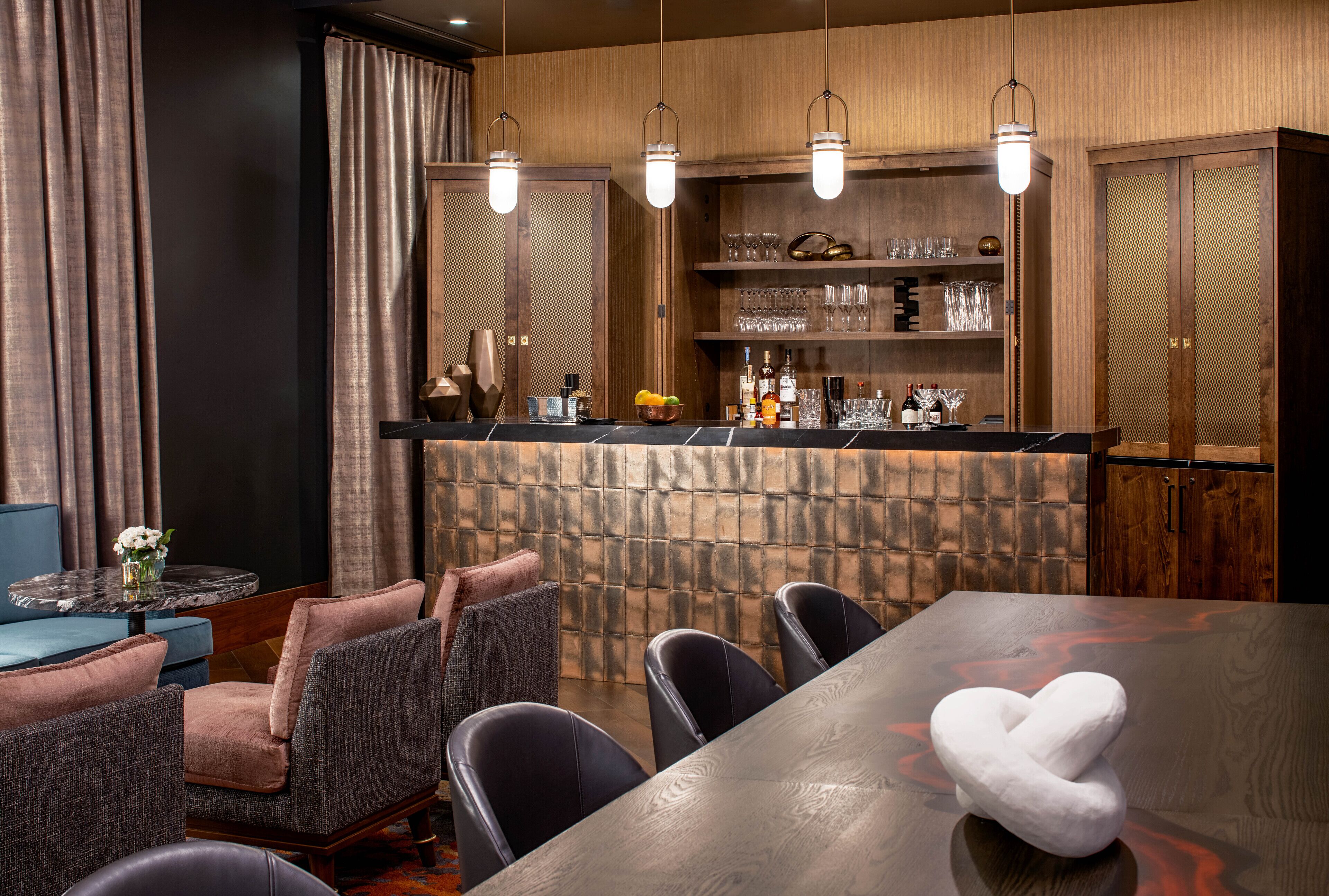Una zona de bar con mostrador de madera, taburetes y un área de estar con mesa y sillas.