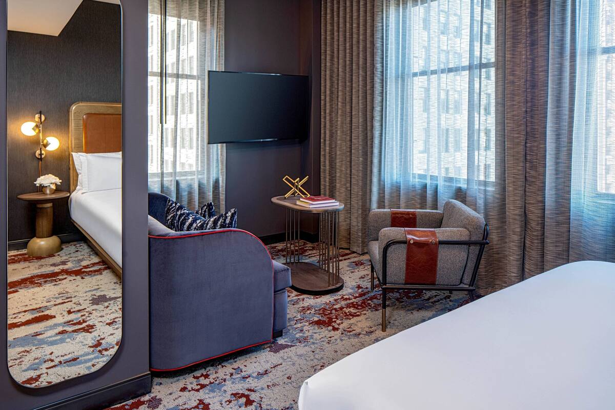 A hotel room with a bed, a sofa, a chair, a TV, and a small table with a lamp.