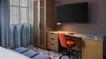 A bedroom with a bed, a desk with a chair, a TV, and a wardrobe.