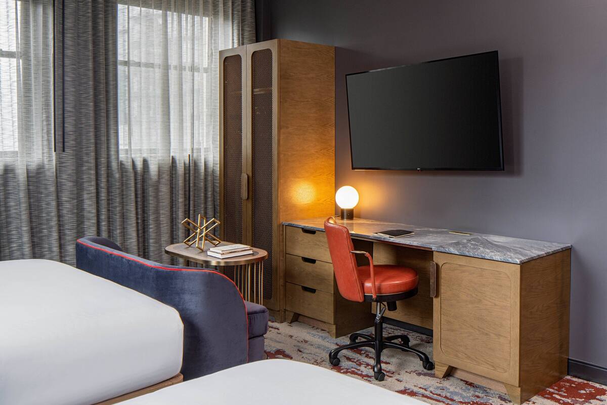A hotel room with a bed, a desk with a chair, a television, and a window with curtains.