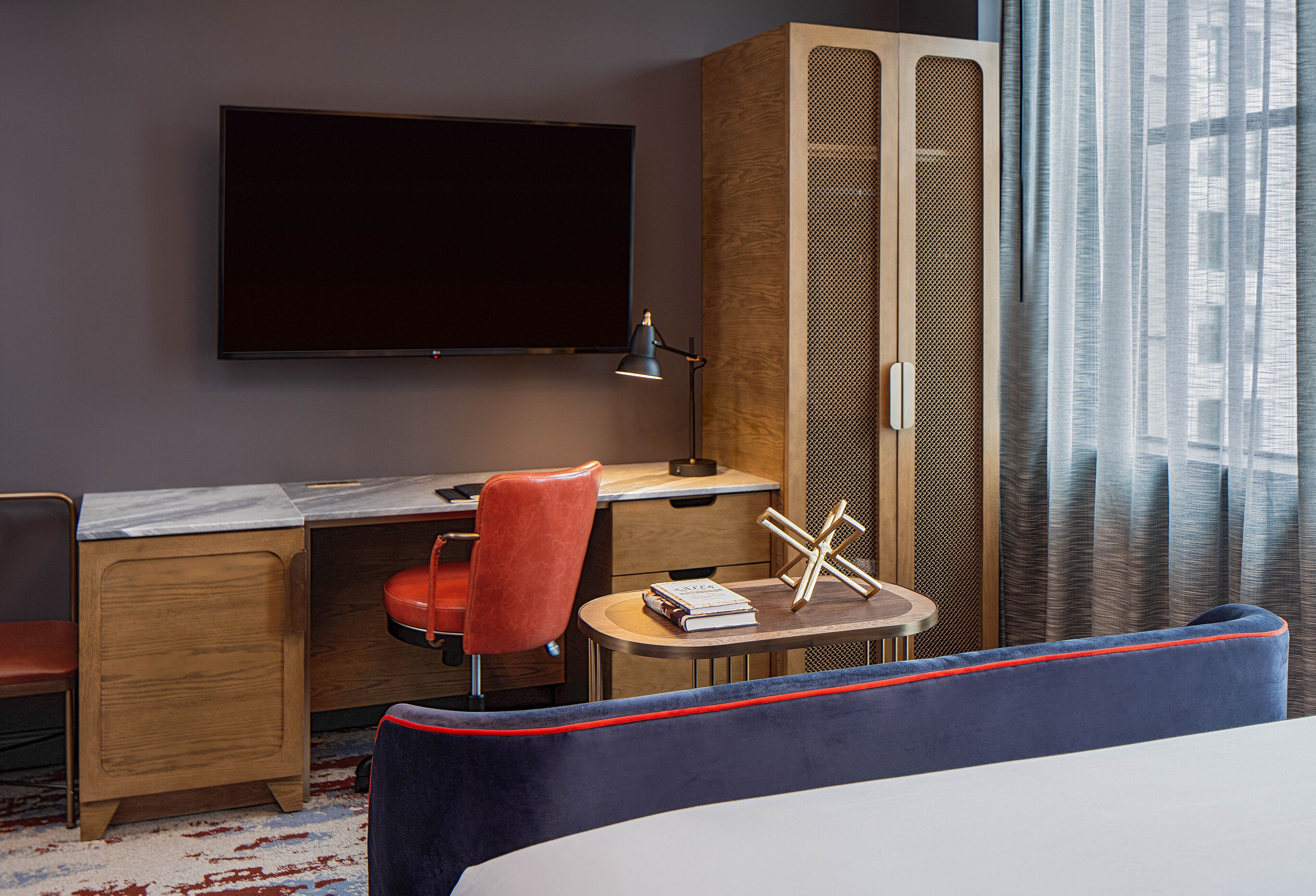 Ein Hotelzimmer mit einem Bett, einem Schreibtisch, einem Stuhl, einem Fernseher und einem Fenster mit Vorhängen.