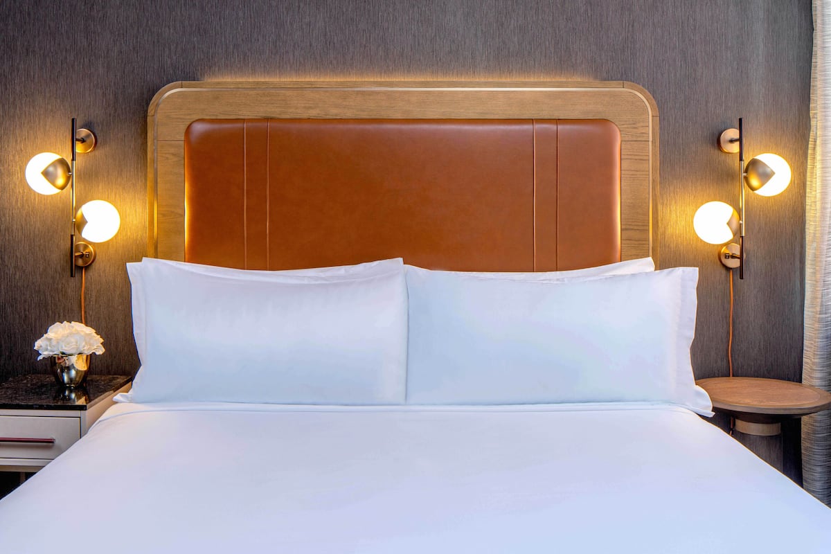 Ein ordentlich bezogenes Bett mit weißen Leinen, ein Holz-Kopfteil und zwei Nachttische mit Lampen.