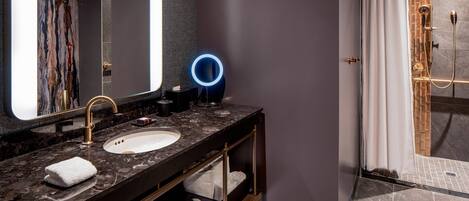 A modern bathroom with a marble sink, a large mirror, a blue illuminated ring light, and a shower area with a glass door.