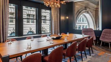 A conference room with a long wooden table, red upholstered chairs, and a chandelier.