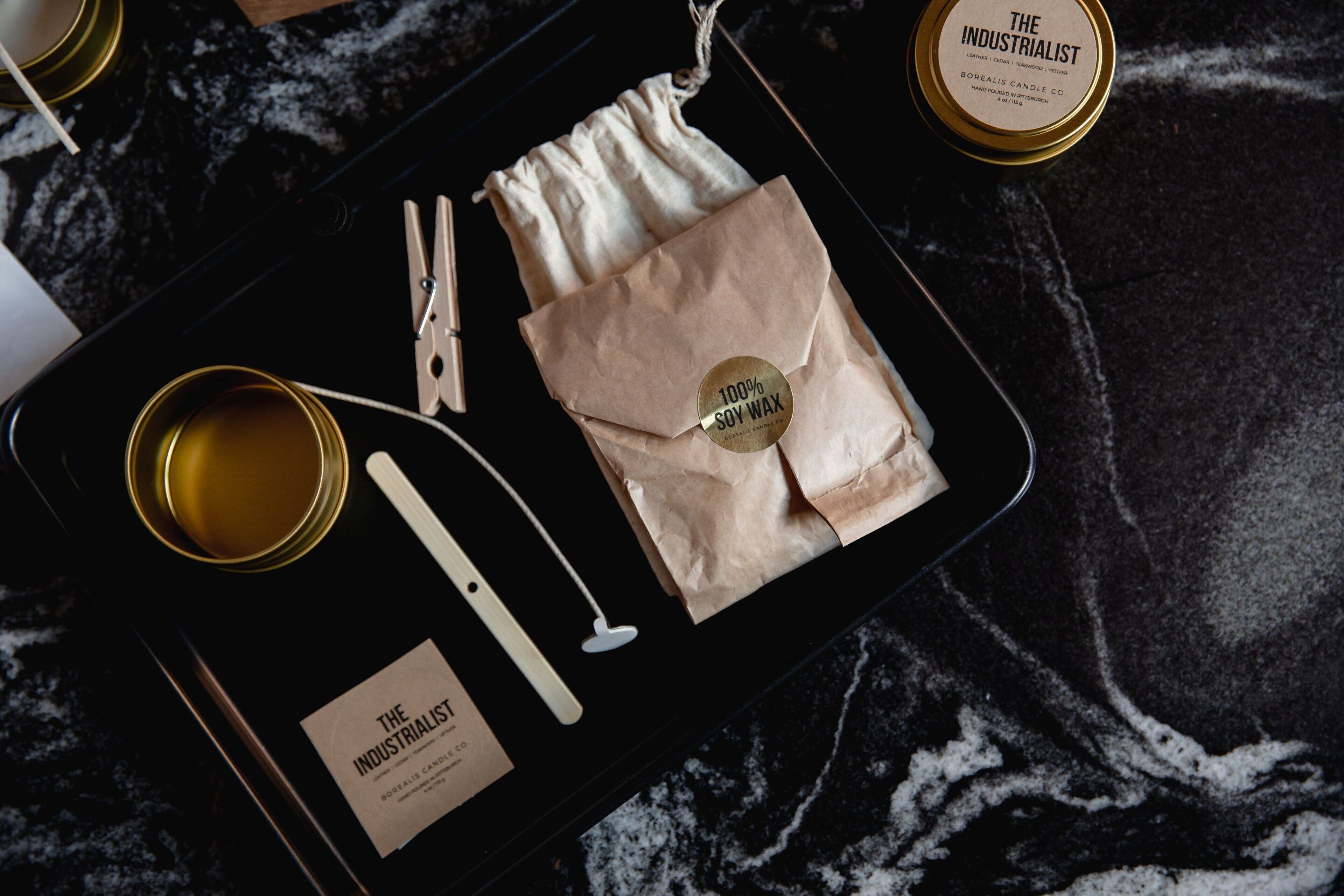 A tray with a candle, clothespins, a cloth, and a tin of soy wax.