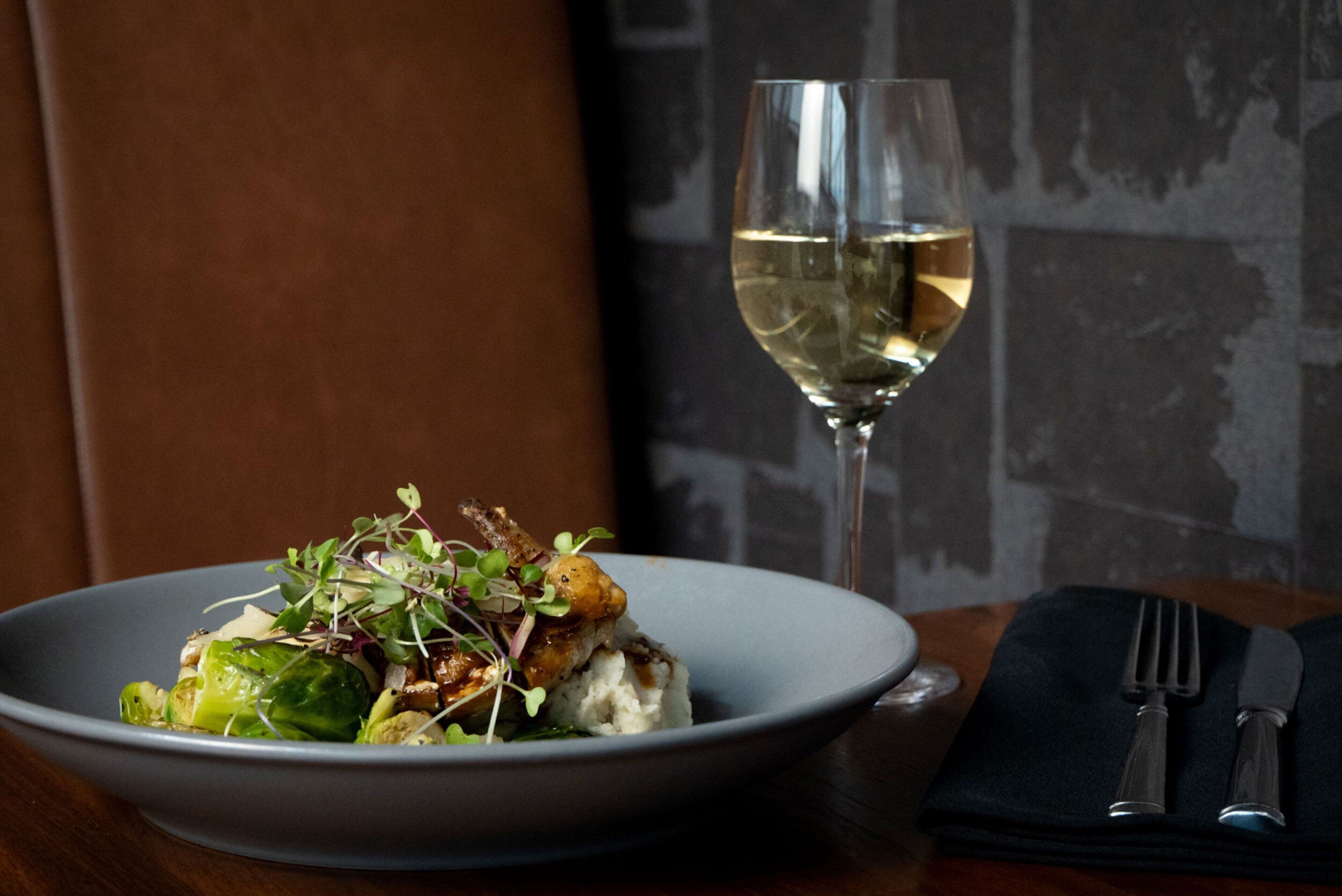 A plate of food with a glass of white wine on a table.