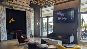 A modern lobby with a neon sign, a large flat-screen TV, and a seating area with a sofa and chairs. - Aloft by Marriott Orlando Lake Buena Vista (Orlando)