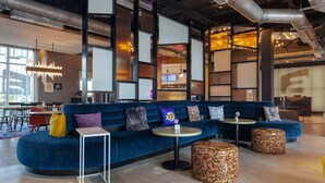 A modern lounge area with a blue sofa, round tables, and patterned ottomans. - Aloft by Marriott Orlando Lake Buena Vista (Orlando)
