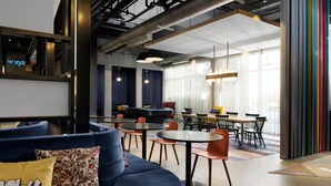 A modern lounge area with a blue sofa, round tables, and chairs, featuring a neon sign and large windows. - Aloft by Marriott Orlando Lake Buena Vista (Orlando)