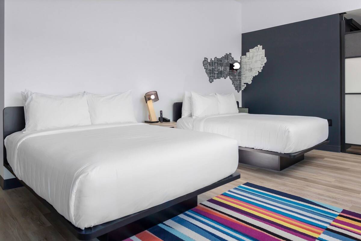 Una habitación de hotel moderna con dos camas, un colorido tapete a rayas y una obra de arte original en la pared.