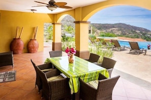 A patio with a table and chairs, a ceiling fan, and a view of a pool and mountains. - Casa Ilan Ilan (Sardinal)